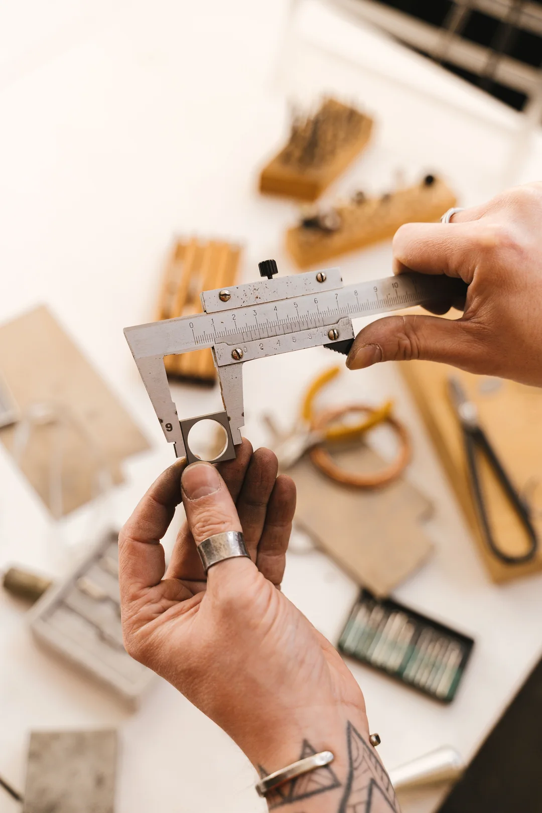 Hands measuring a ring with a caliper at a jewellery workbench.